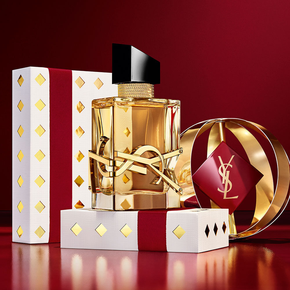 Frasco iconico de LIBRE destacado con cajas de regalo YSL en burdeos y oro de lujo.