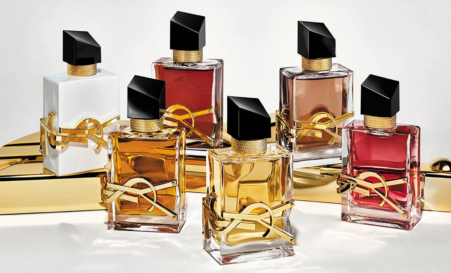 Dos fragancias del perfume YSL Libre se presentan sobre una superficie dorada brillante. Los frascos presentan variaciones en el color del líquido y el acabado, incluyendo tonos transparentes, blancos, rosados ​​y marrones. Todos lucen las icónicas letras YSL en dorado y una fuente negra inclinada.

