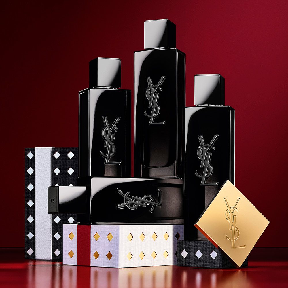 Frascos de YSL MYSLF Eau de Parfum apilados sobre estuches de regalo festivos con motivos negros y plateados.