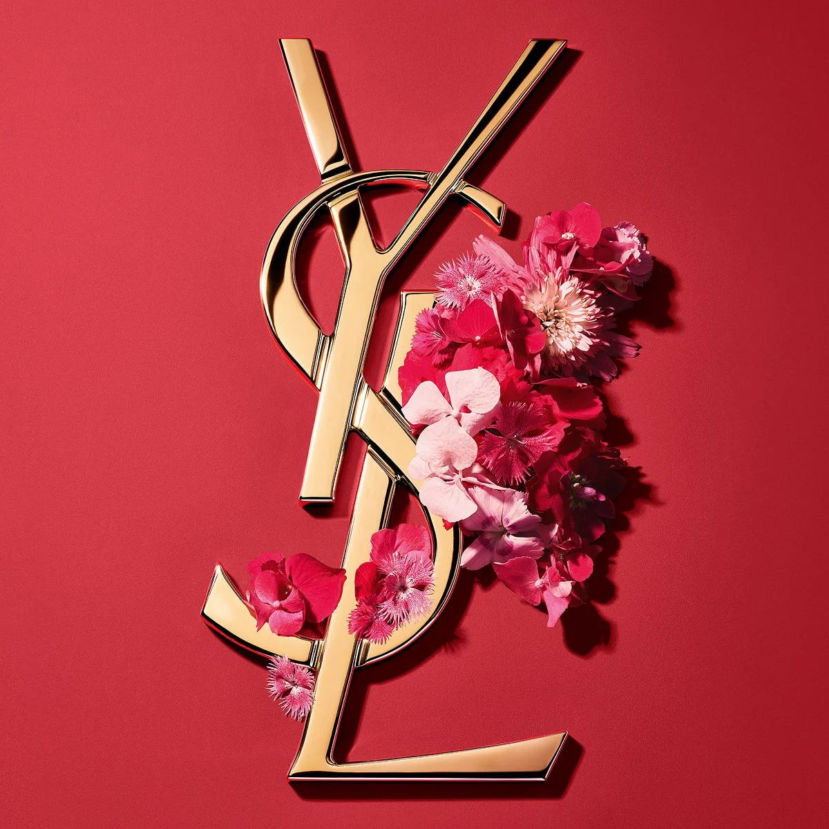 Logotipo Cassandre dorado de YSL, adornado con vibrantes flores rosas primaverales, sobre un fondo rosa.