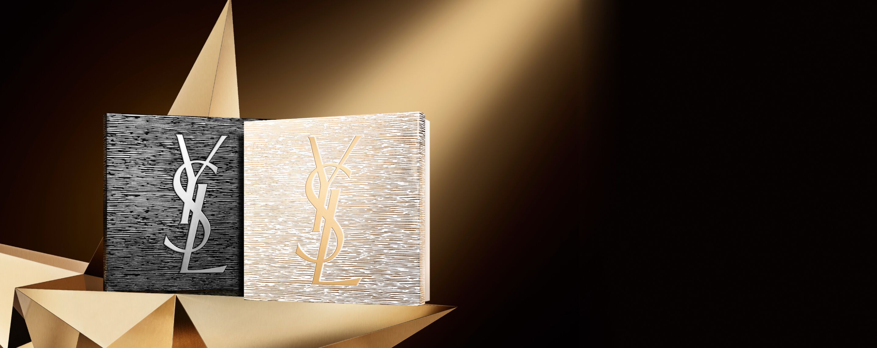 Dos elegantes juegos de regalo navideños de YSL Beauté, uno negro con un logotipo plateado y otro dorado con un logotipo dorado, colocados sobre una superficie dorada geométrica, que insinúan alta costura y brillo.