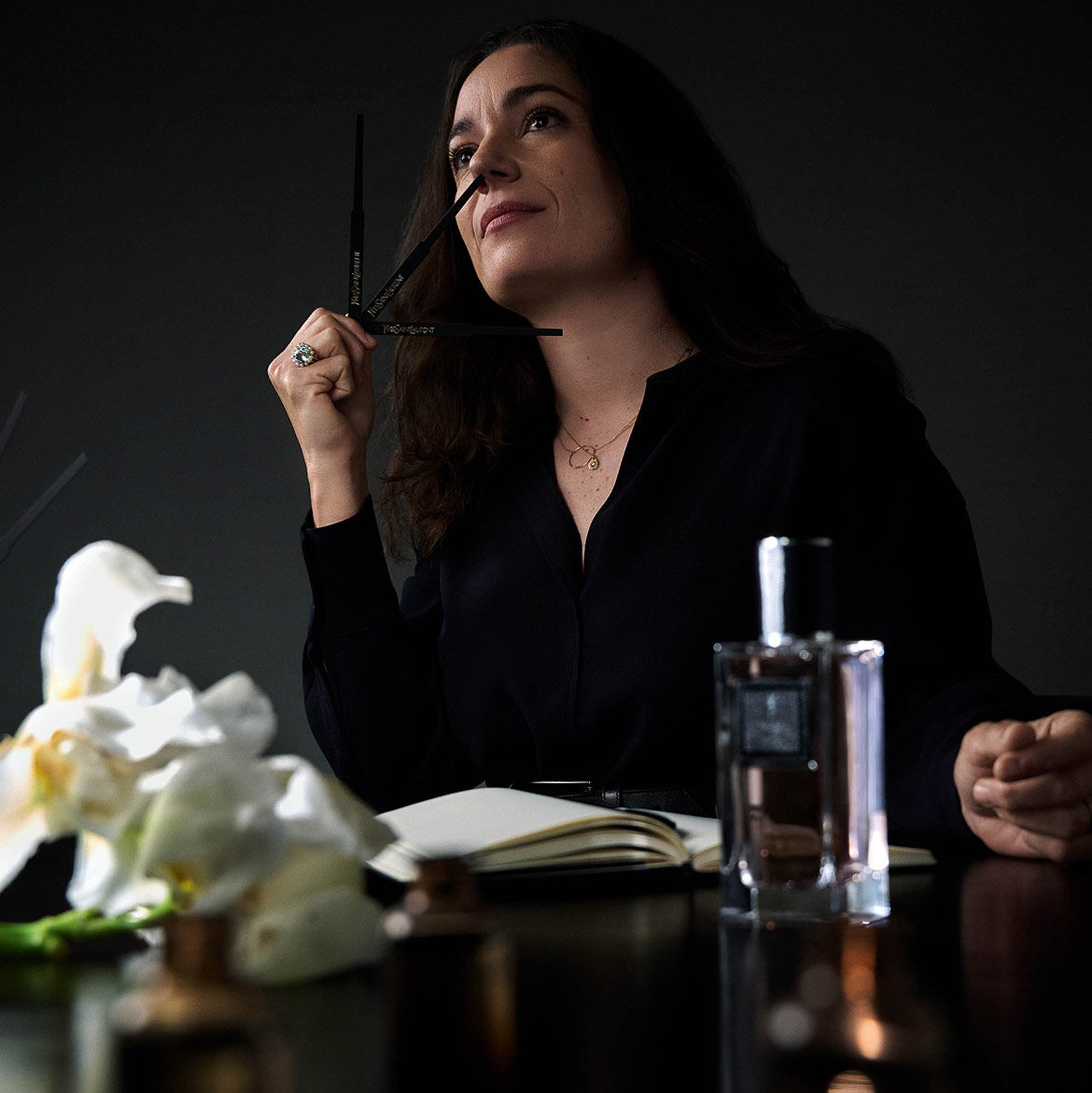 Mujer oliendo tiras de perfume, con una libreta y un frasco de perfume.