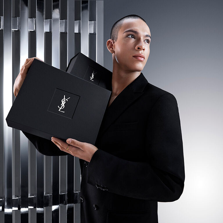 Pierre-Antoine, un modelo masculino, sostiene con elegancia una sofisticada caja de regalo negra de YSL Beauty con el icónico logo Cassandre.