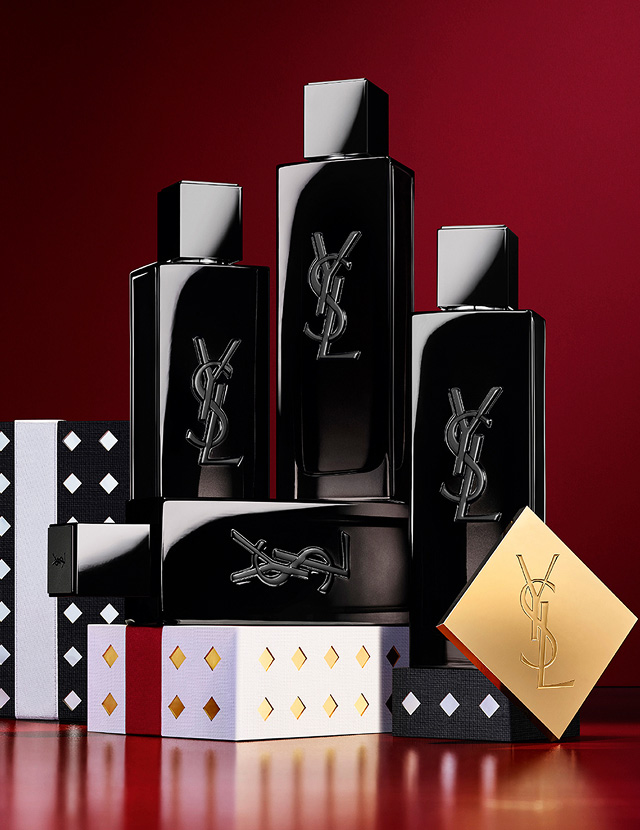 Frascos de YSL MYSLF Eau de Parfum apilados sobre estuches de regalo festivos con motivos negros y plateados.