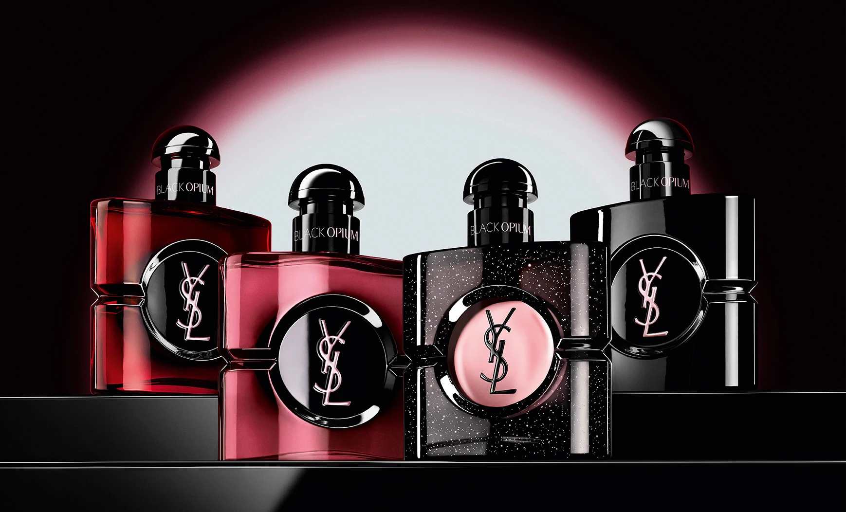 Cuatro frascos diferentes de perfume Black Opium colocados en fila sobre una superficie oscura y reflectante.
