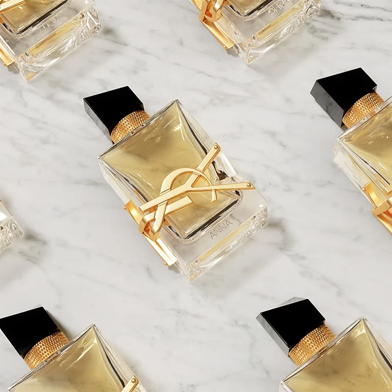 Frascos de perfume YSL Libre personalizados con grabados de nombres, dispuestos sobre mármol blanco.