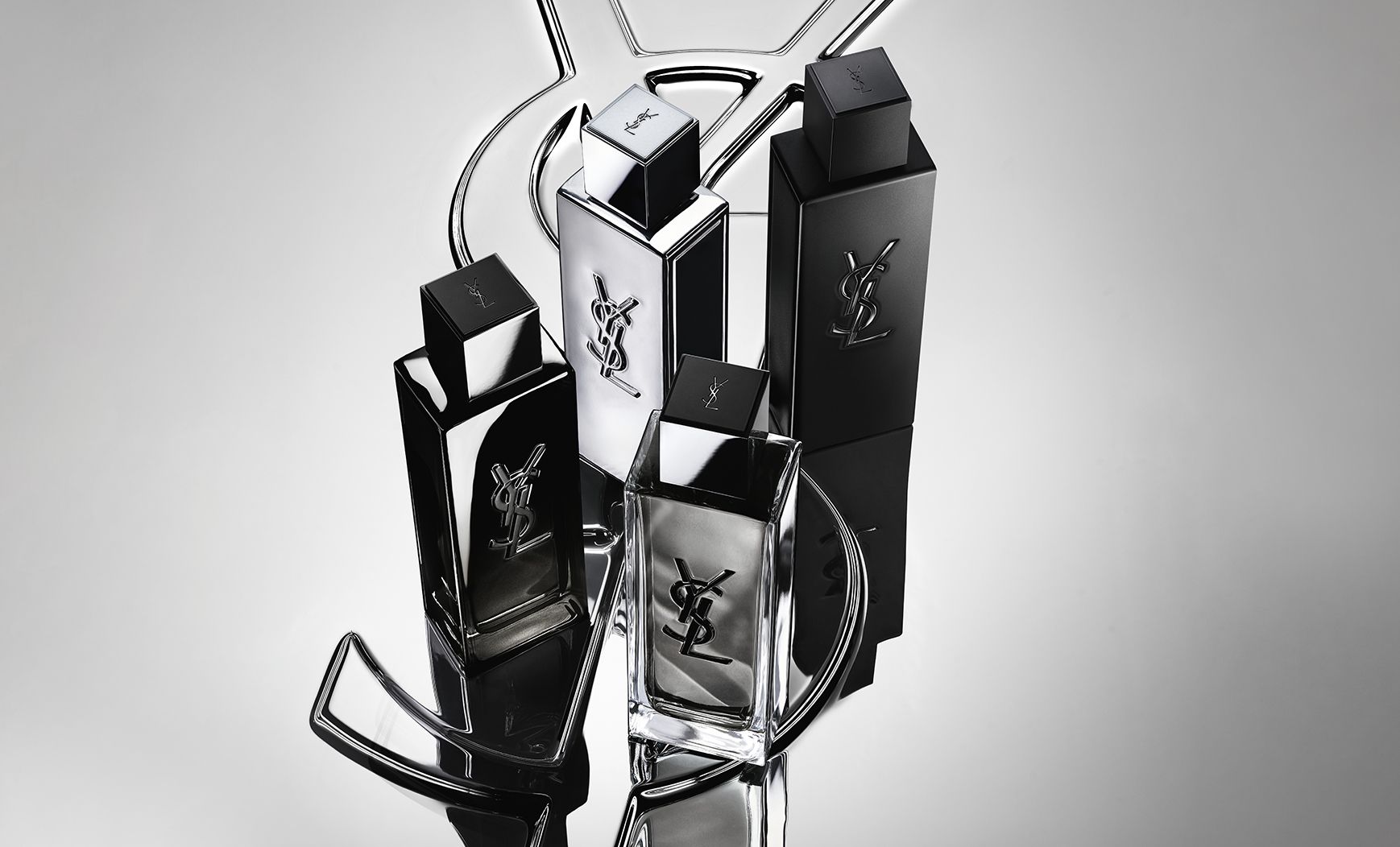 Imagen de grupo de toda la gama de fragancias MYSLF, con los frascos colocados sobre un gran logotipo Cassandre de YSL con efecto espejo reflectante.