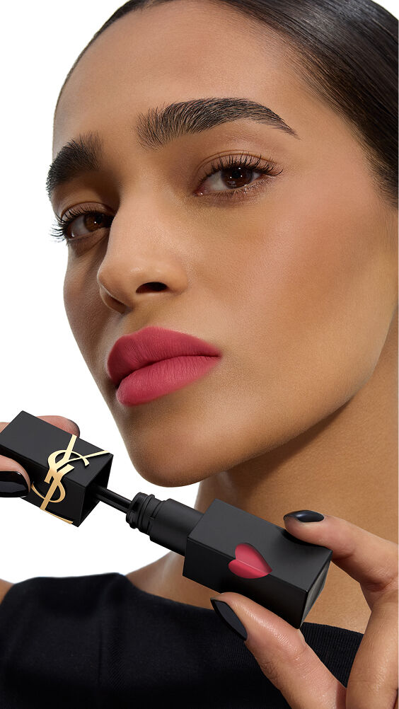 Modelo de tono de piel medio con un color labial rosa-mate vibrante, sosteniendo el frasco negro de YSL THE INKS BLUR con su corazón rosa.
