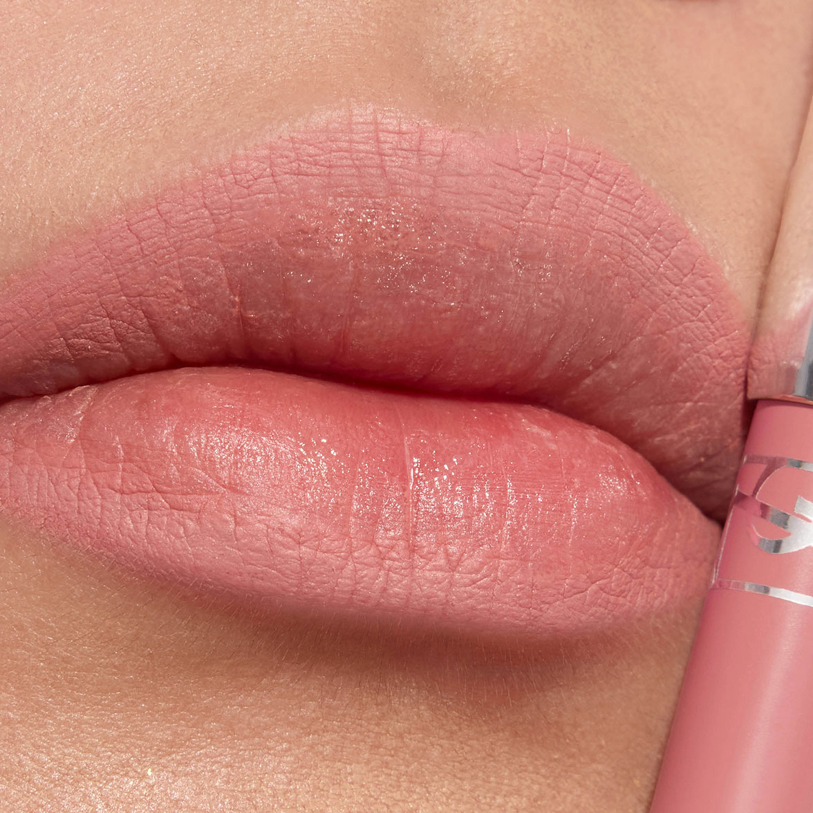 Primer plano de unos labios con labial mate rosa suave y su aplicador a juego.