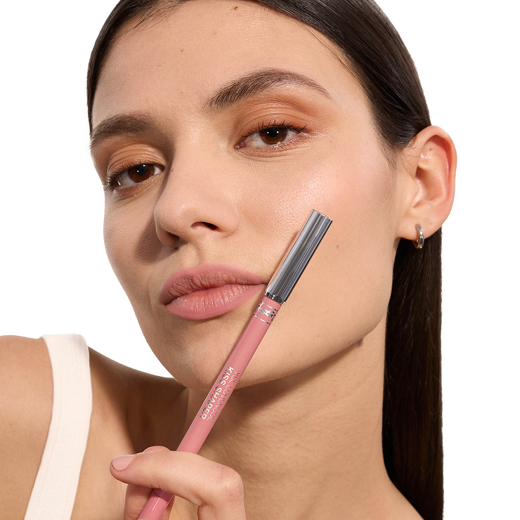 Primer plano de una modelo con labios mate rosa suave sosteniendo un perfilador YSL Kiss Shaper a juego.