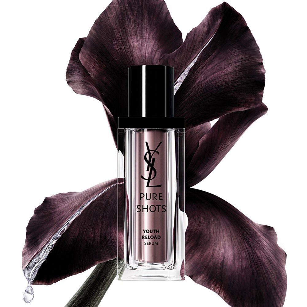 Botella de YSL Beauty Pure Shots Youth Reload Serum, elegantemente posicionada frente a una flor de iris púrpura oscuro.