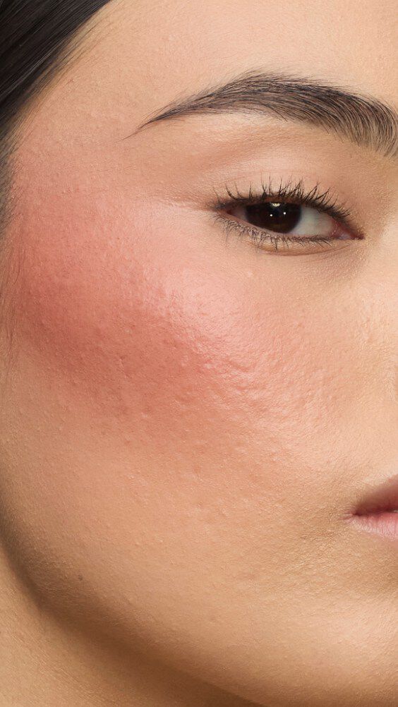 Primer plano del pómulo de una modelo con la rutina Make Me Blush: Polvo #37 Peachy Nude superpuesto con Crema #90 Toffee Temptation para un resplandor bañado por el sol.