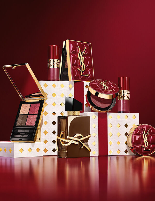 Colección de maquillaje y cofre regalo de fragancias YSL Navidad 2026 sobre pedestales blancos con puntos dorados en burdeos.