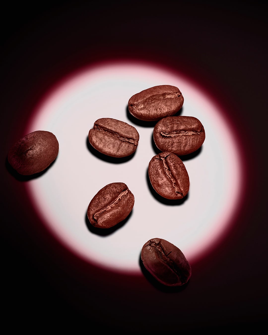 Un grupo de granos de café tostados realzado por un foco circular rosa sobre un fondo oscuro.