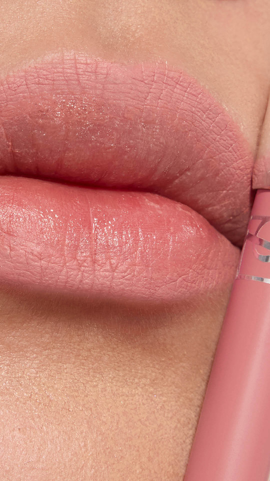 Primer plano vertical de unos labios con labial mate rosa suave y su aplicador a juego.