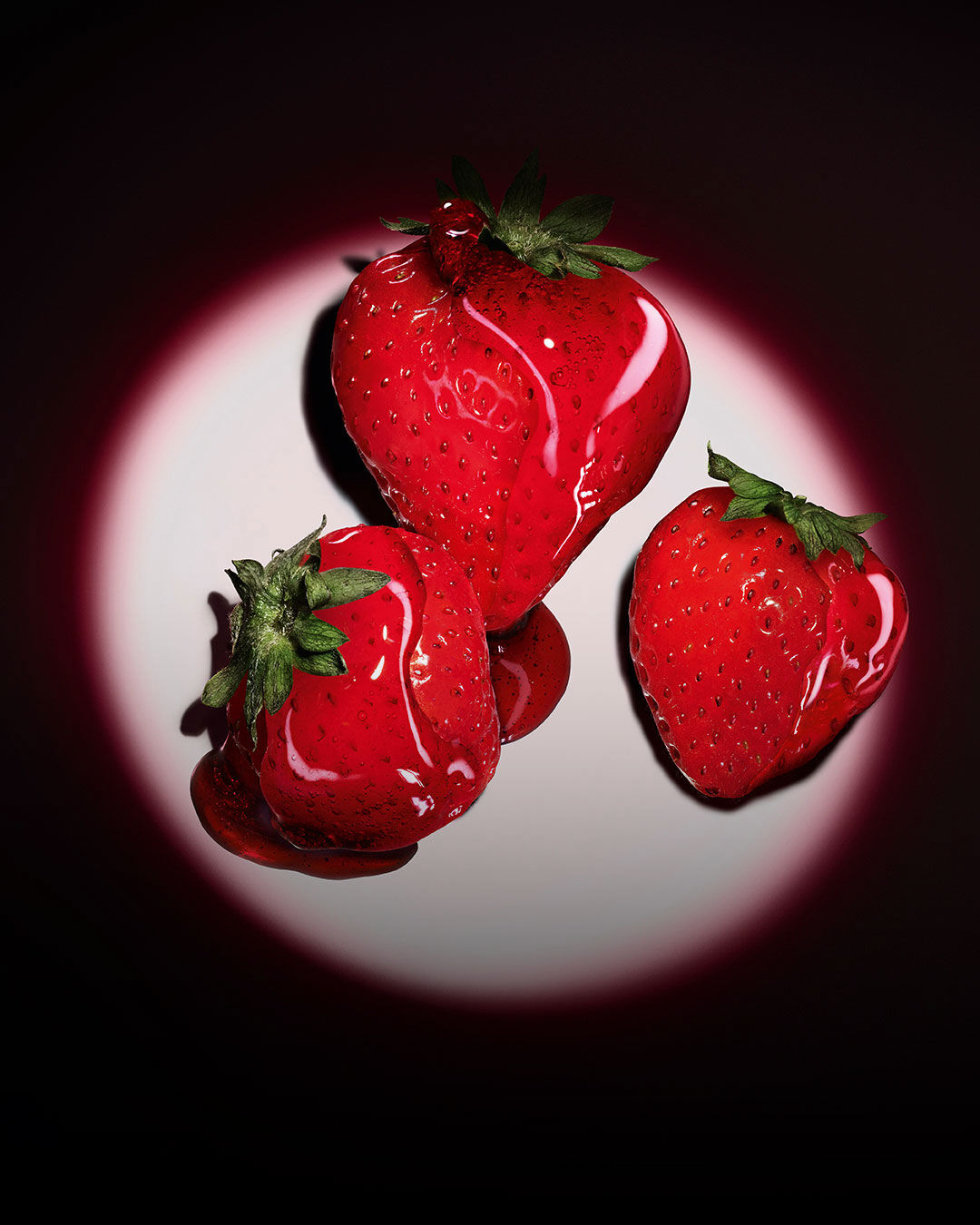 Tres fresas rojas resaltadas por un foco circular rosa sobre un fondo oscuro.