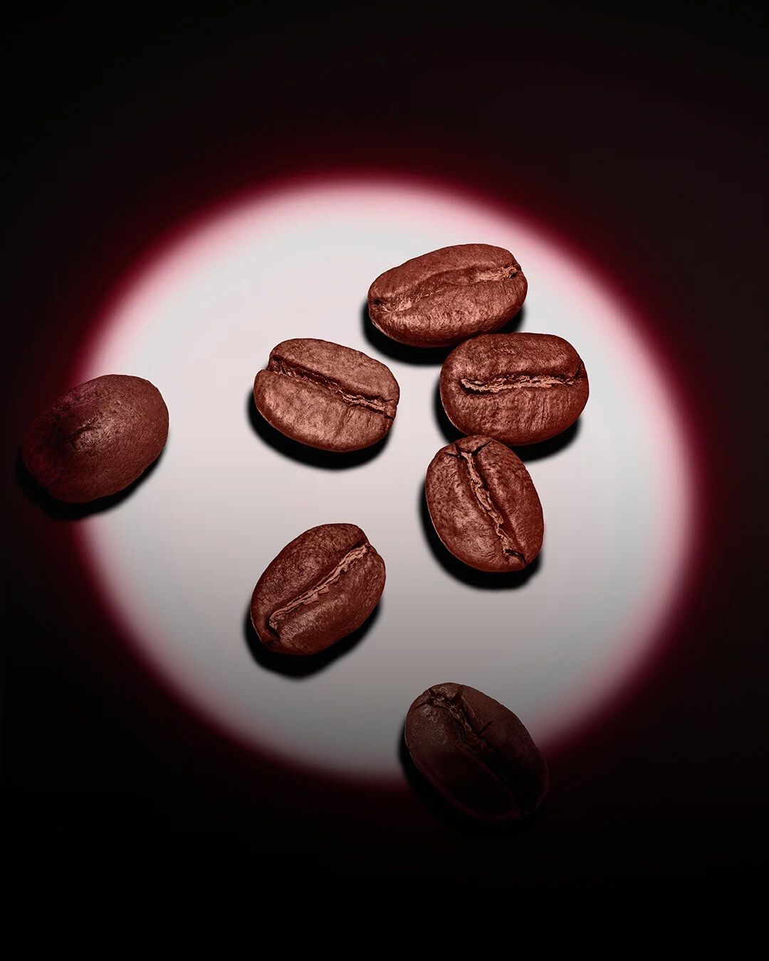 Un grupo de granos de café tostados realzado por un foco circular rosa sobre un fondo oscuro.