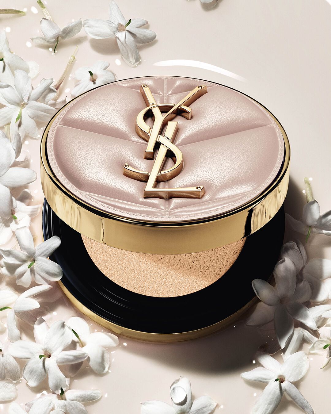 Primer plano de YSL SKIN AFFAIR SOFT GLOW CUSHION en un charco de base líquida y flores de jazmín. Acabado radiante y sensorial.
