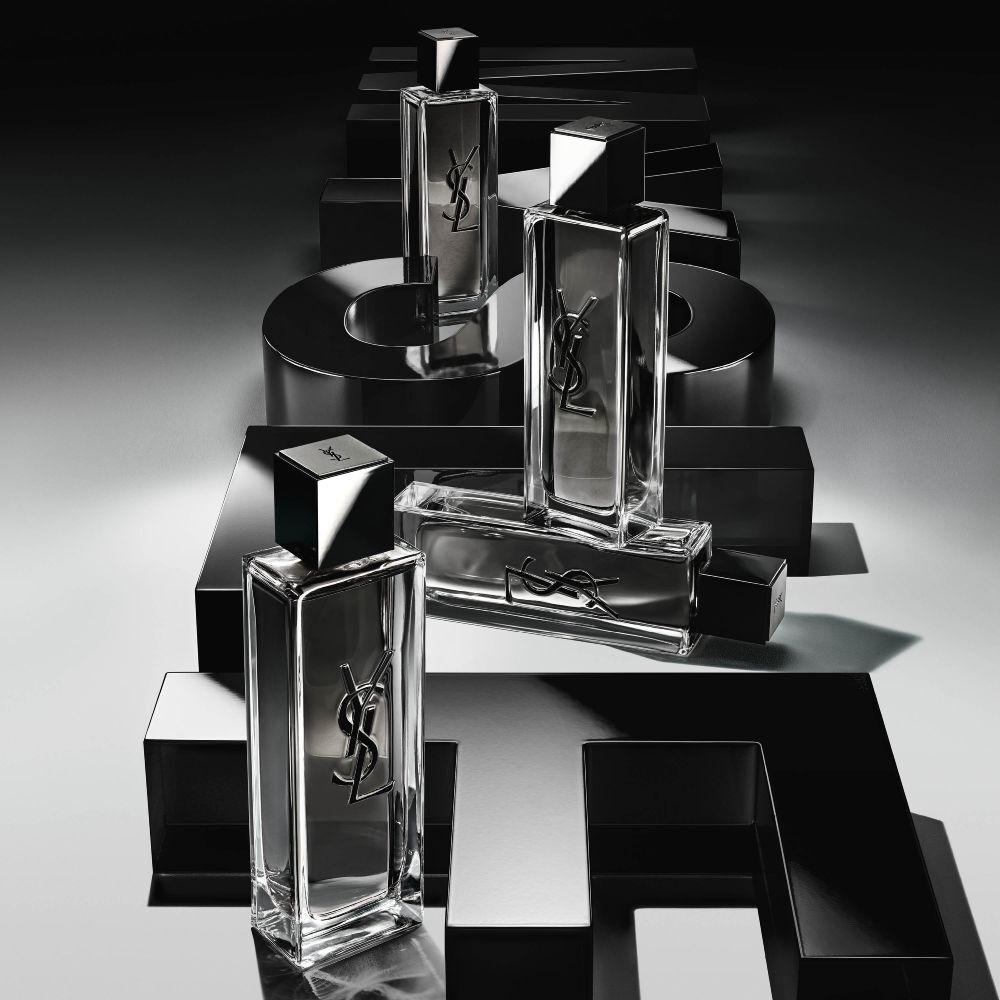 Vista en picado de varios frascos de MYSLF Eau de Toilette Intense dispuestos sobre grandes letras negras en 3D que forman la palabra MYSLF, colocadas sobre el suelo.