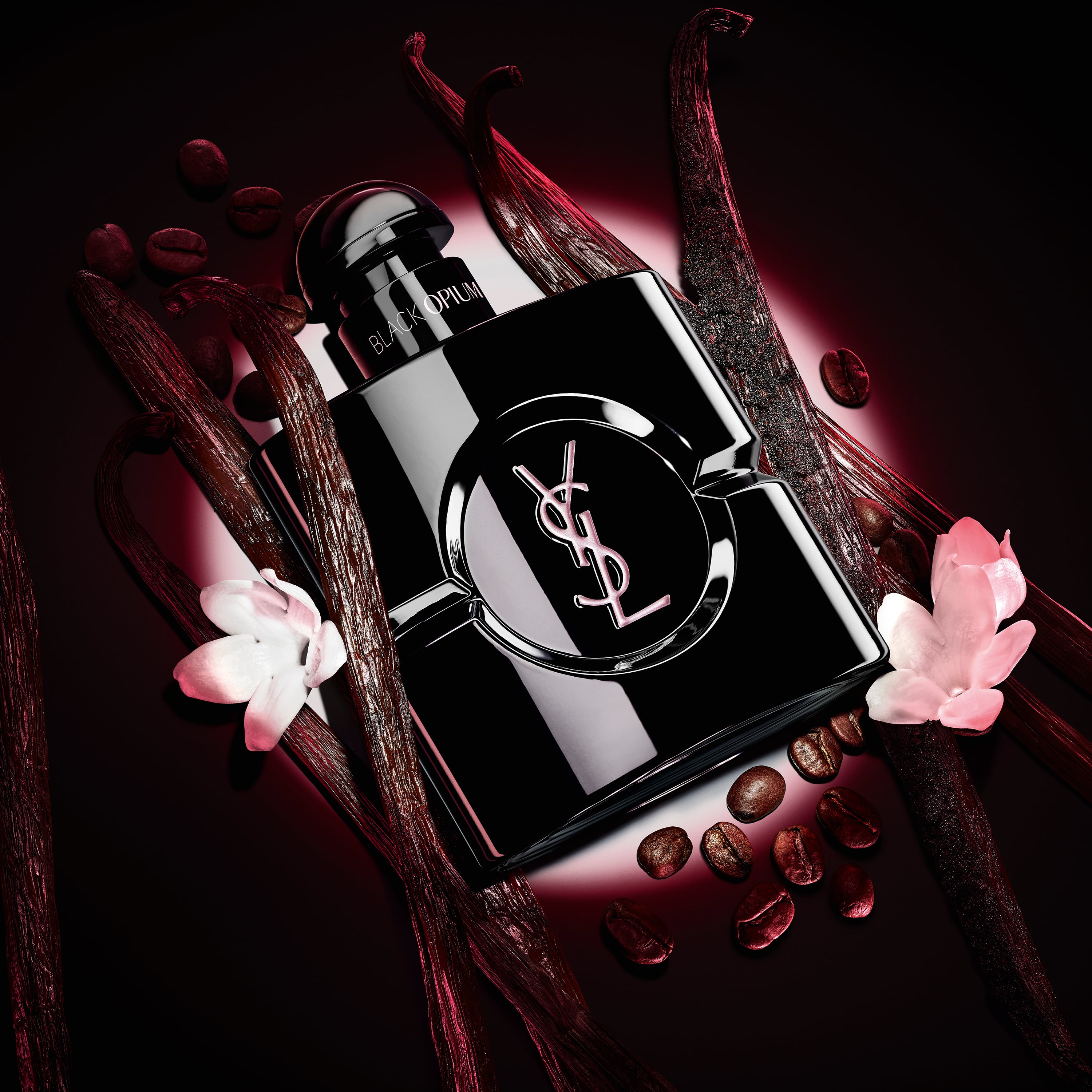 Frasco de Black Opium Le Parfum en negro brillante, rodeado de oscuras vainas de vainilla y jazmín blanco.