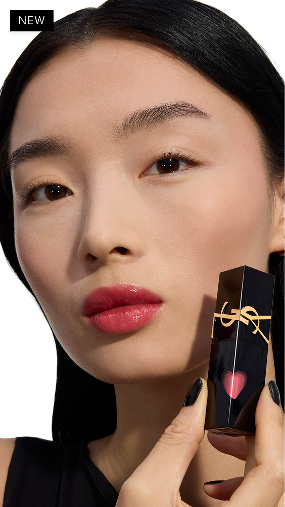 Modelo de tono de piel claro con un look labial brillante en rosa baya, sosteniendo el frasco negro de la mancha labial YSL THE INKS VINYL CREAM con su corazón rojo brillante.