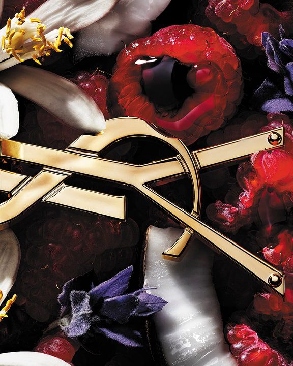 Logo de YSL rodeado de frambuesas, flores blancas y moradas, y coco.