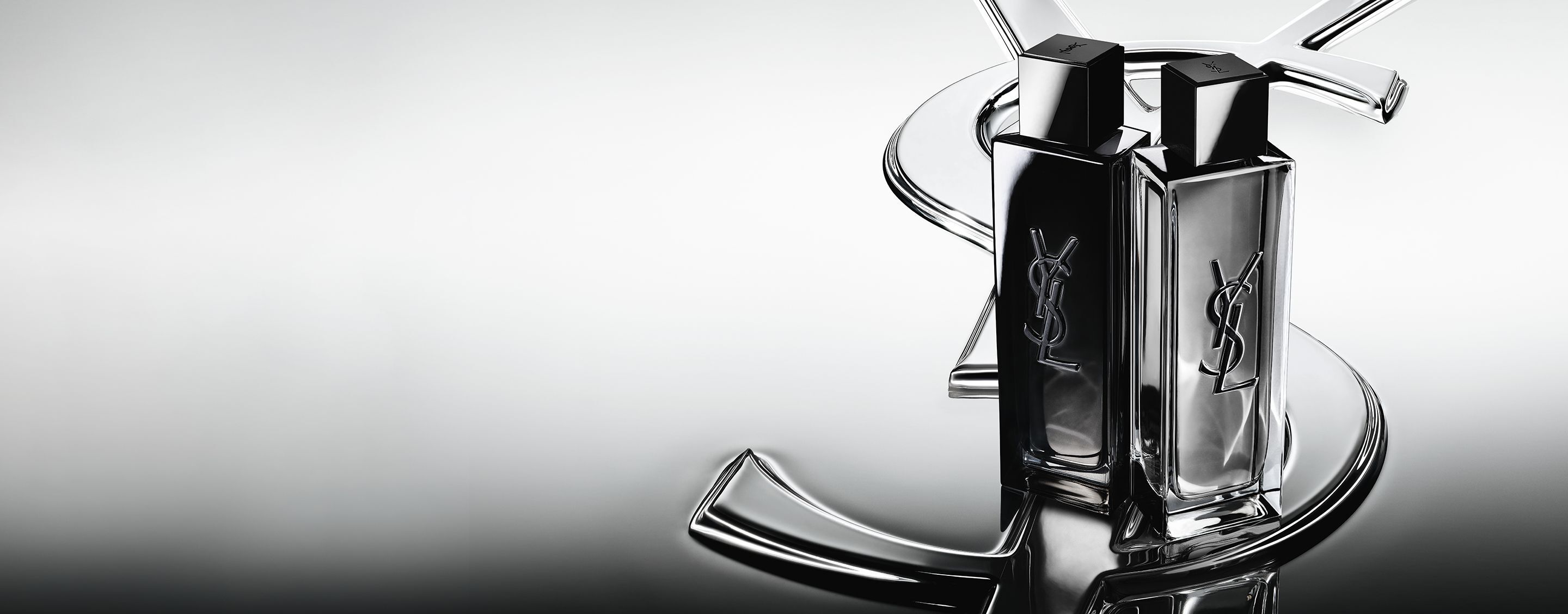Los frascos de MYSLF Eau de Parfum y MYSLF Eau de Toilette Intense, colocados uno junto al otro sobre un gran logotipo Cassandre de YSL con efecto espejo.