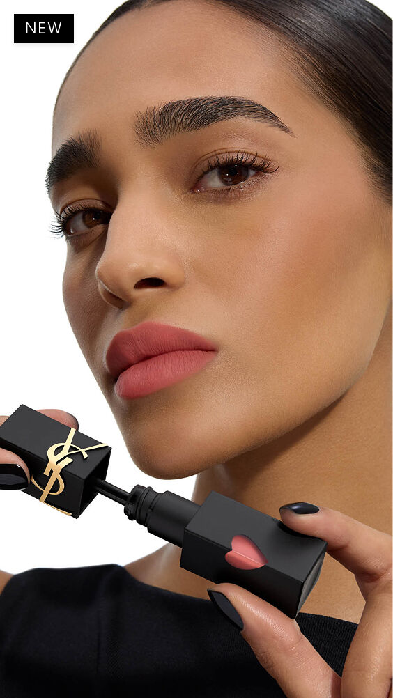 Modelo de tono de piel medio-profundo con un look labial mate de enfoque suave, sosteniendo el aplicador de la mancha de labios YSL THE INKS BLUR junto a su mentón.