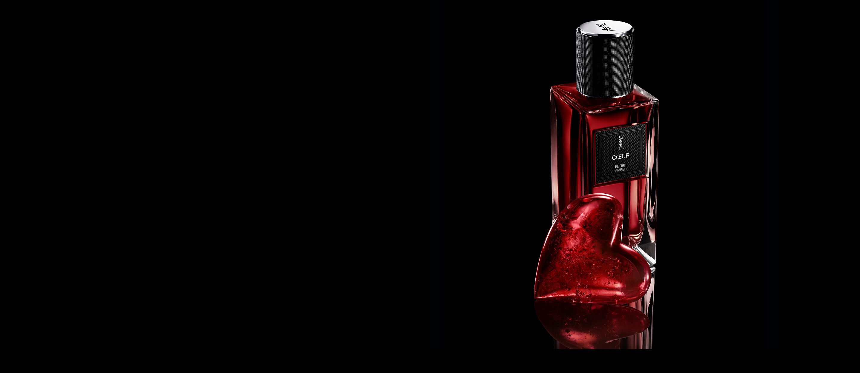 Frasco de CŒUR Eau de Parfum de YSL
junto a una joya de corazón rojo rubí sobre una
superficie negra reflectante.