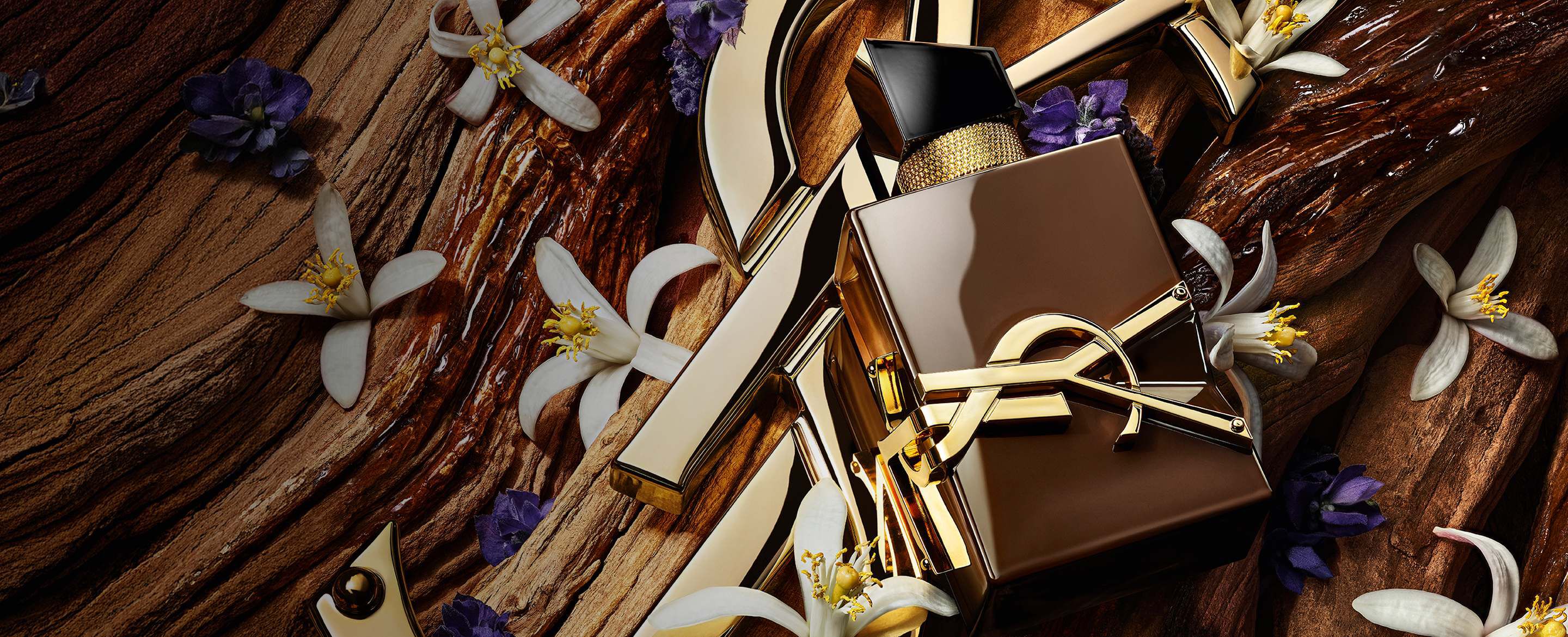 Frasco de Libre Santal Couture en marrón glaseado que refleja la luz, colocado sobre una gran Cassandre YSL dorada.