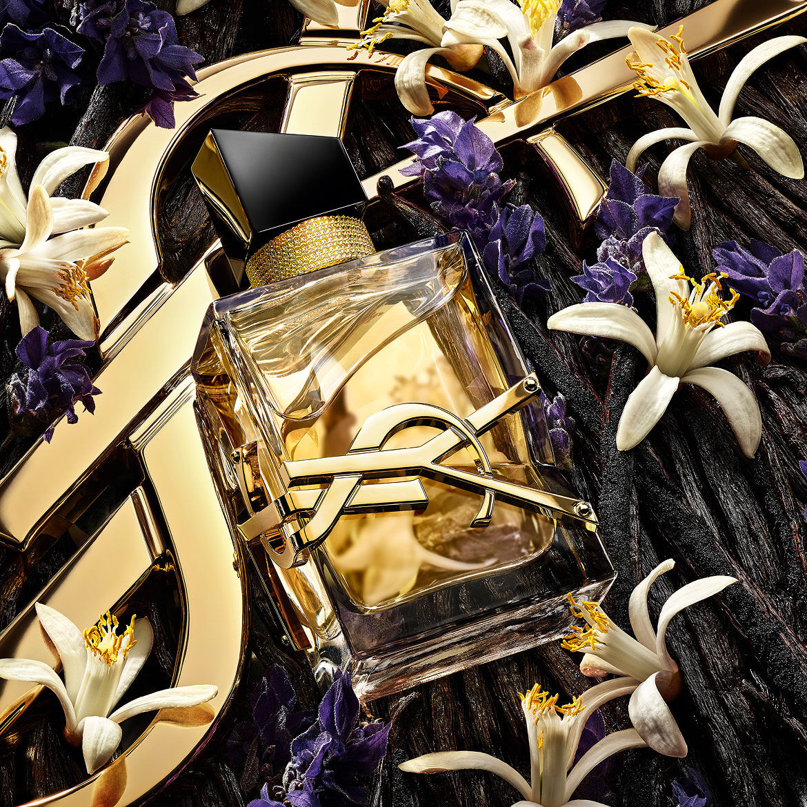 El frasco de perfume Libre centrado entre una mezcla de flores de lavanda, azahar y vainas de vainilla sobre un fondo dorado de YSL.