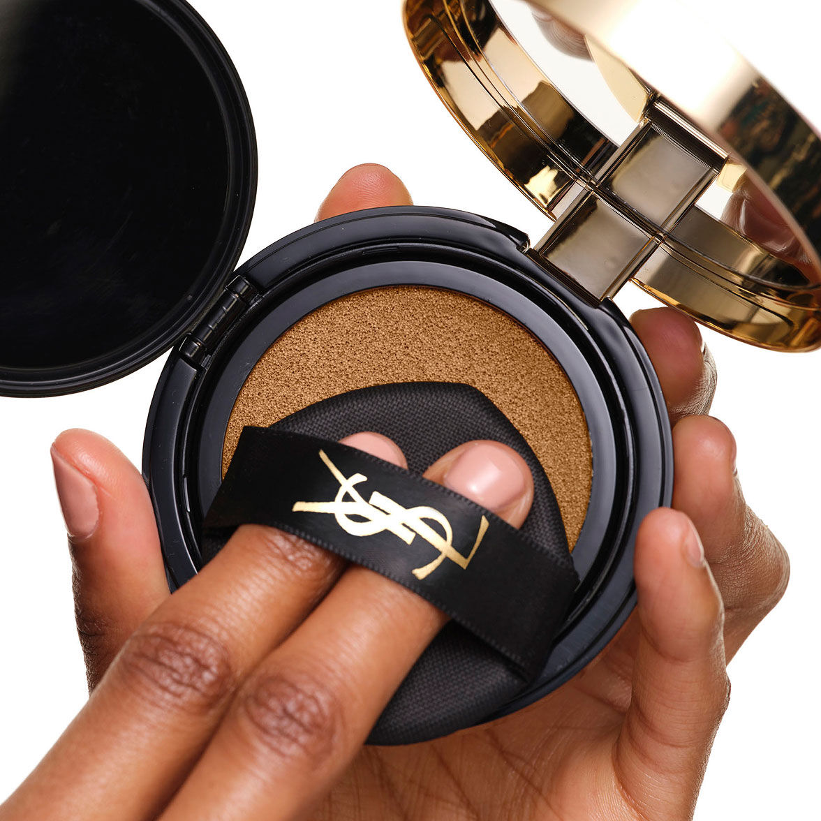 Cargando el YSL SKIN AFFAIR SOFT GLOW CUSHION. Dedos bajo la cinta negra con el logo, presionando la esponja aplicadora de maquillaje.