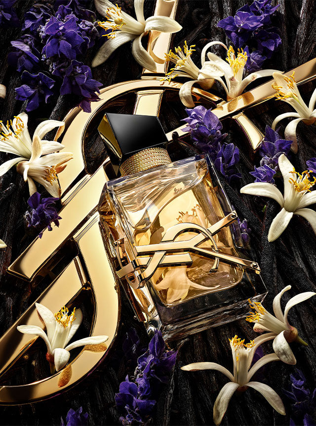 El frasco de perfume Libre centrado entre una mezcla de flores de lavanda, azahar y vainas de vainilla sobre un fondo dorado de YSL.