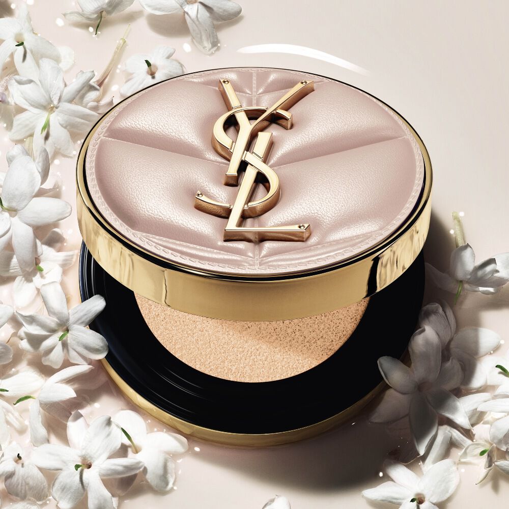 Primer plano de YSL SKIN AFFAIR SOFT GLOW CUSHION en un charco de base líquida y flores de jazmín. Acabado radiante y sensorial.