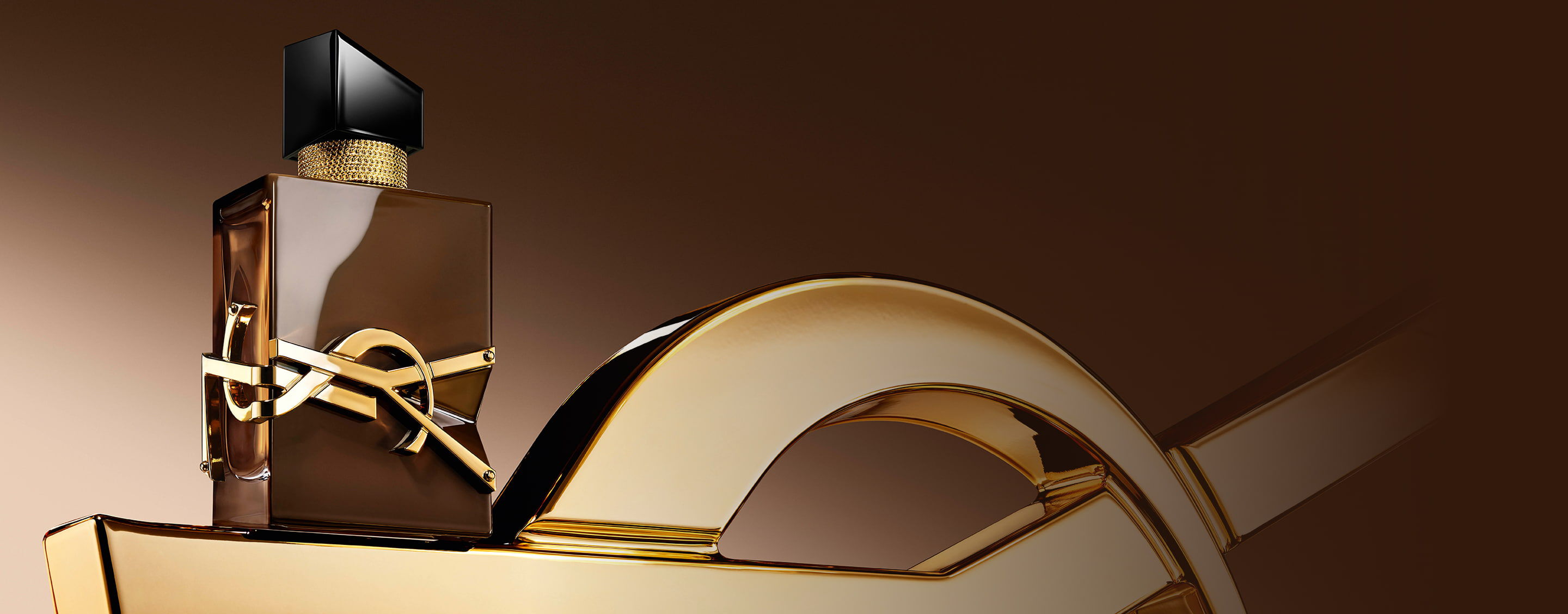 Frasco Libre Santal Couture en marrón glaseado que refleja la luz, dispuesto sobre una gran Cassandre YSL dorada.