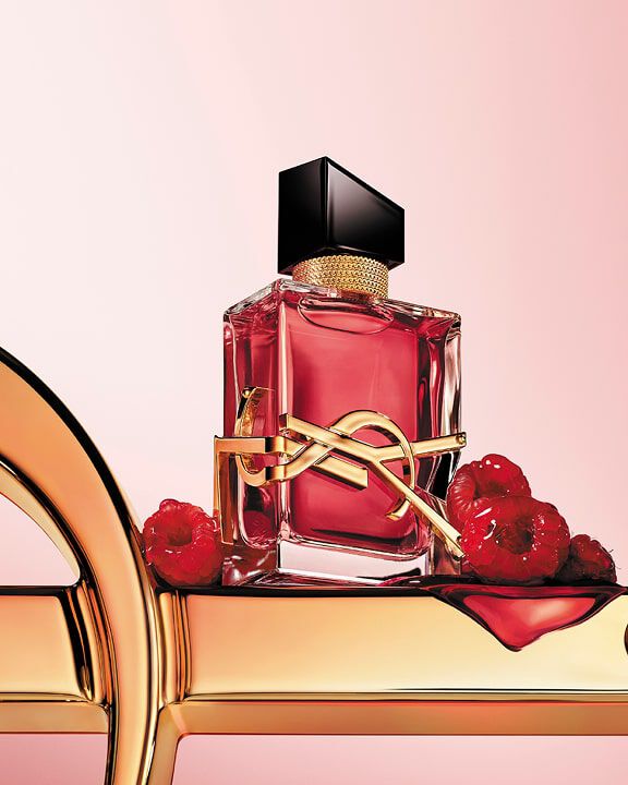 Frasco de perfume YSL rojo con logo dorado, sobre una superficie dorada con frambuesas.