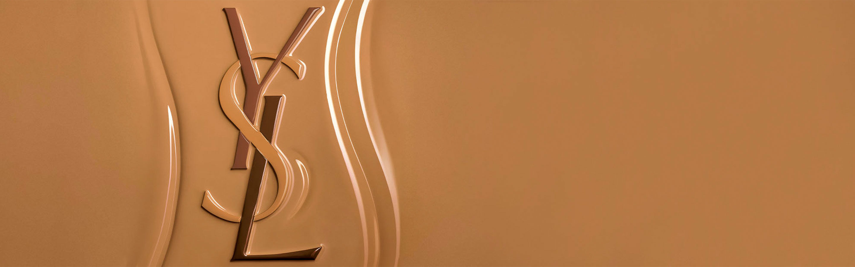 Logotipo de Yves Saint Laurent (YSL) en relieve sobre una superficie texturizada de base de maquillaje líquida, resaltando la consistencia rica y fácil de difuminar del producto.