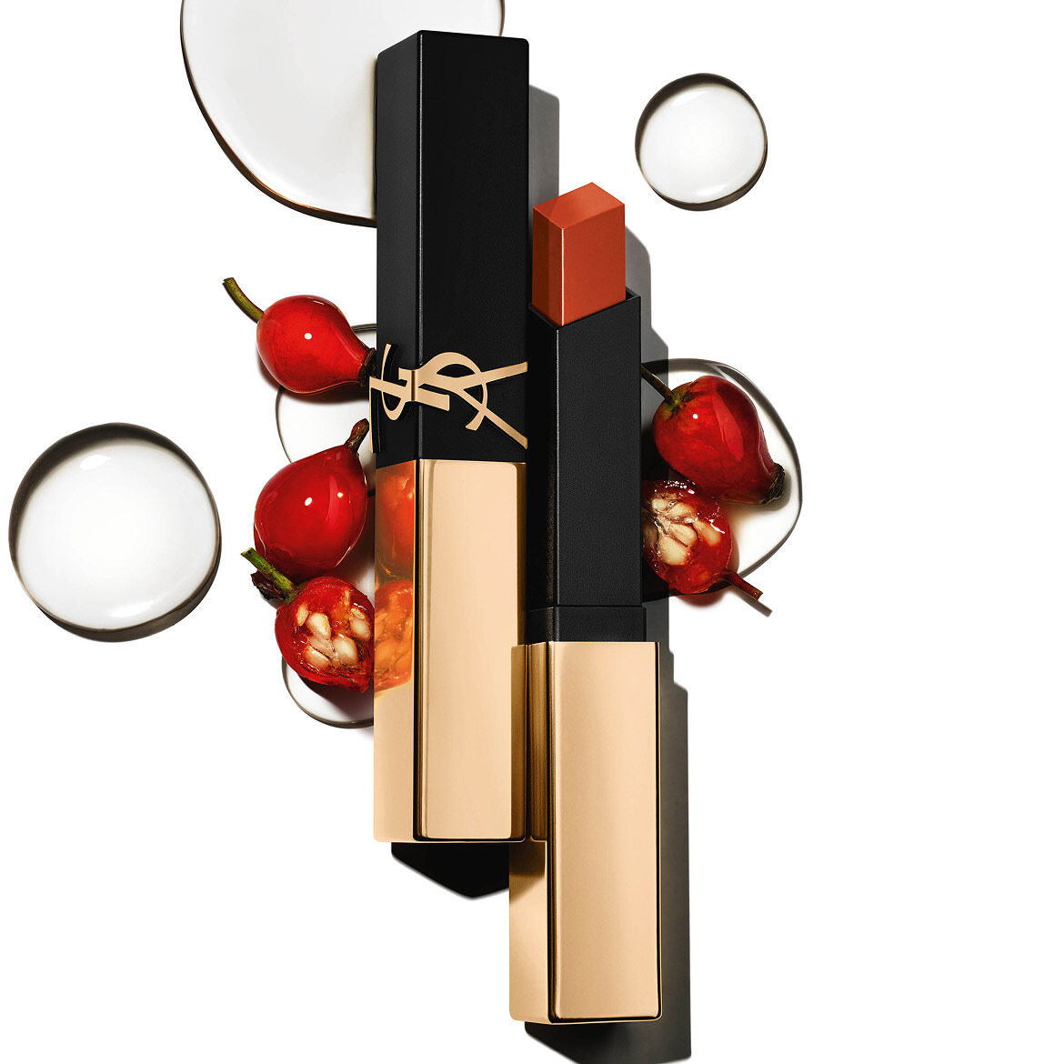 Labial cuadrado de YSL con tapa dorada, rodeado de bayas rojas y gotas transparentes sobre blanco.